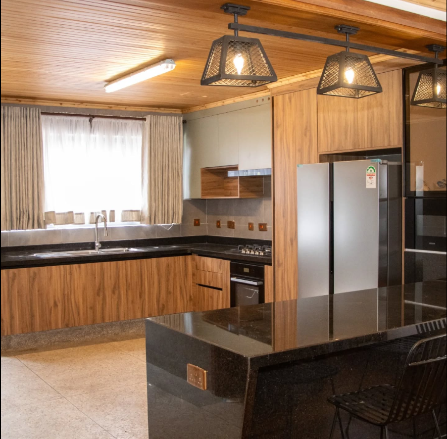 Warm timber kitchen with wooden ceiling, patterned pendant lights and a black granite island